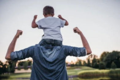 Man with child on shoulders outdoors, flexing muscles